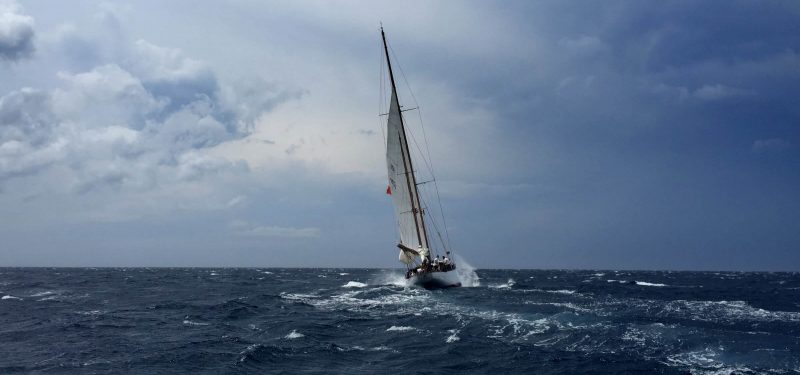 White sail boat, tacking into the headwind, on a body of water.