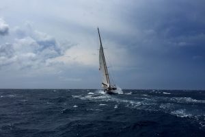 White sail boat, tacking into the headwind, on a body of water.